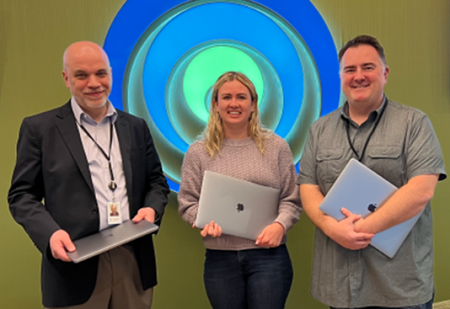 Three smiling people holding laptops