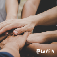 A group of people bring their hands together in a stacked circle, the Cambia logo is in the bottom left corner and in white font