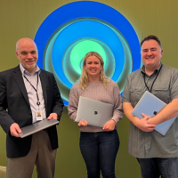 Three smiling people holding laptops