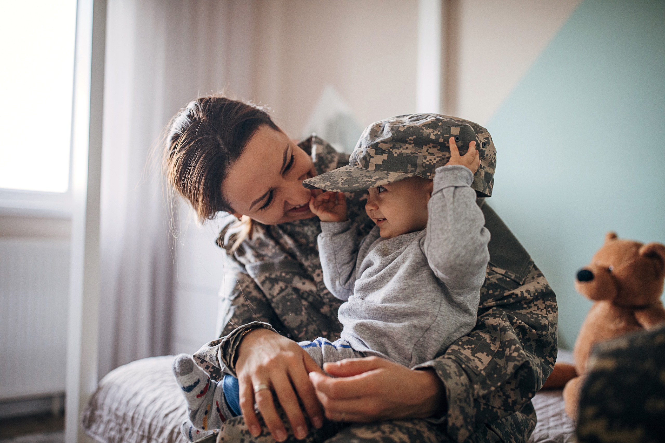 Woman wearing camouflage holding a smiling baby wearing her hat