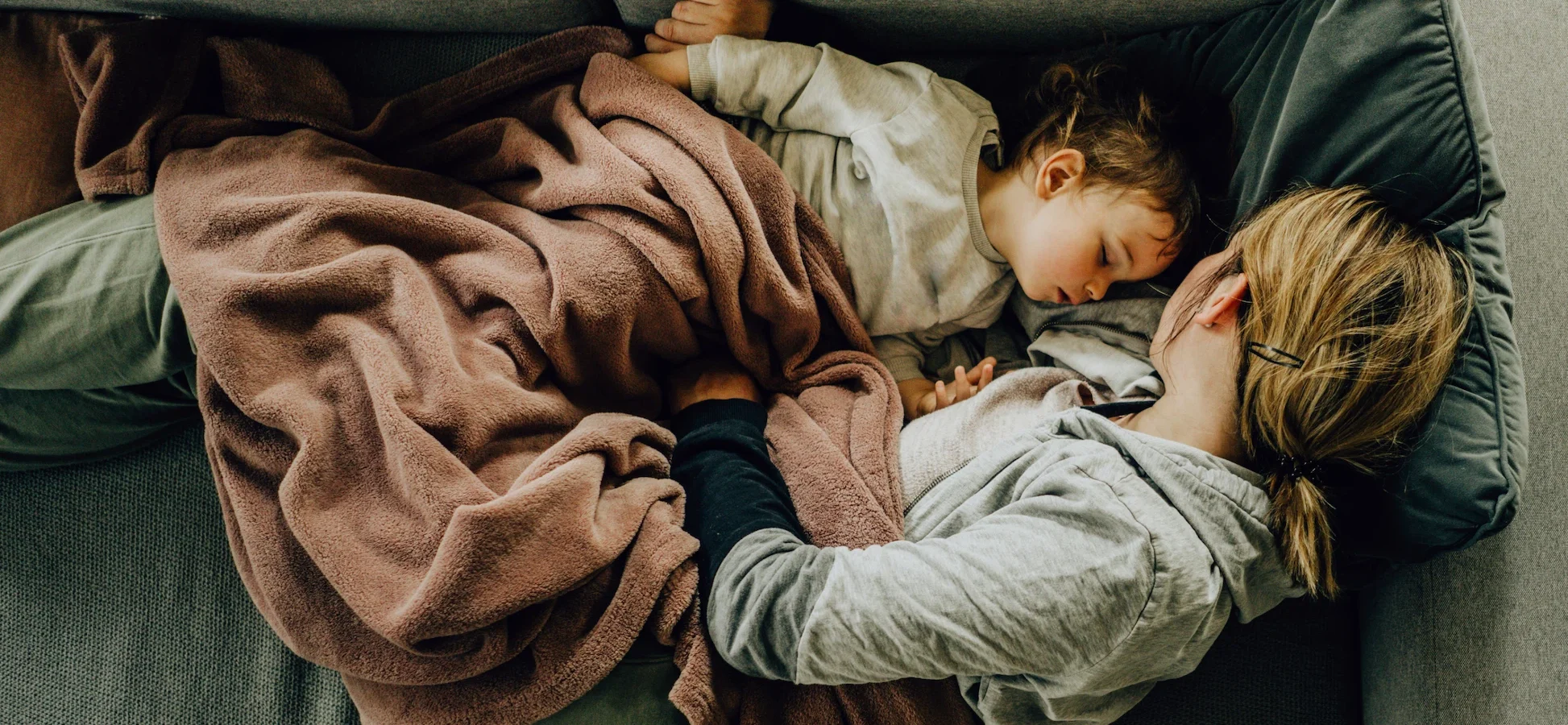 Woman and young child sleeping on couch with blanket